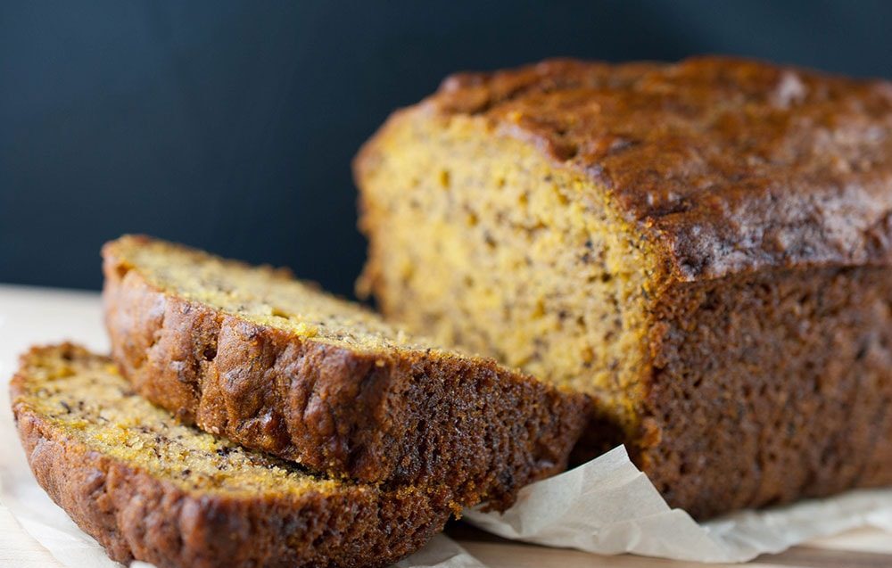 A freshly baked pumpkin banana loaf topped with a light glaze, sliced on a wooden cutting board.